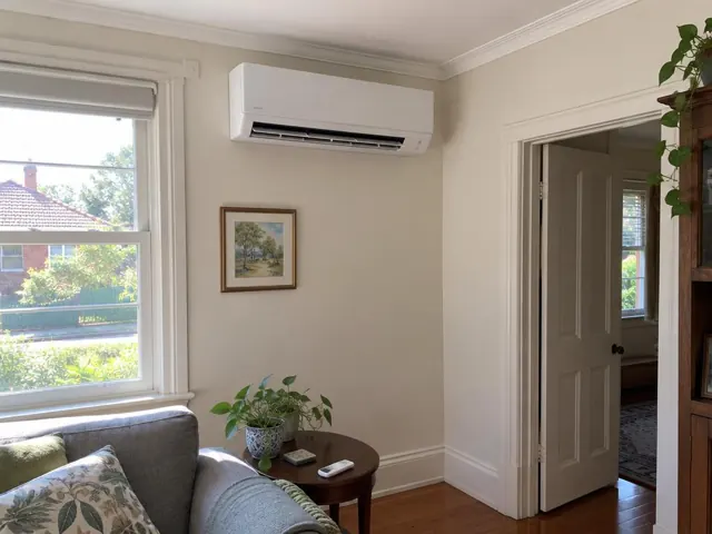 Clean indoor split system on a cream wall in a lived-in lounge room with window, doorway and timber floor in Plympton