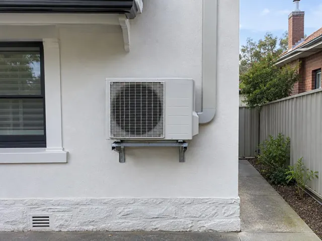 Outdoor air conditioner unit mounted on a wall bracket beside a home exterior in Edwardstown